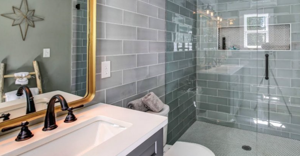 Глянцевая плитка серых цветов и стеклянная перегородка в ванной визуально увеличивают длину помещения