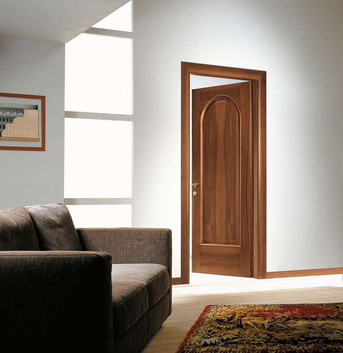 Двери из массива в интерьере гостиной с плинтусами и наличниками орехового цвета на фоне светлых стен